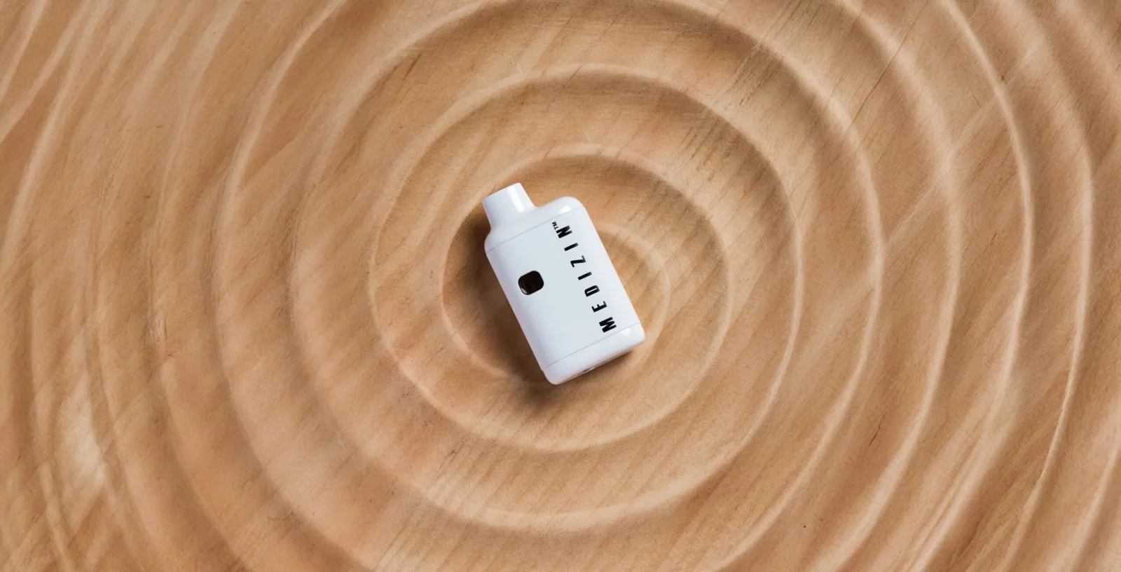 A Medizin all-in-one vape on a carved wooden tray