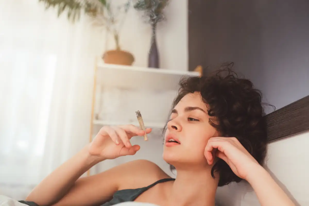 Cropped view of the cute young curly woman smoking cannabis at the modern bedroom