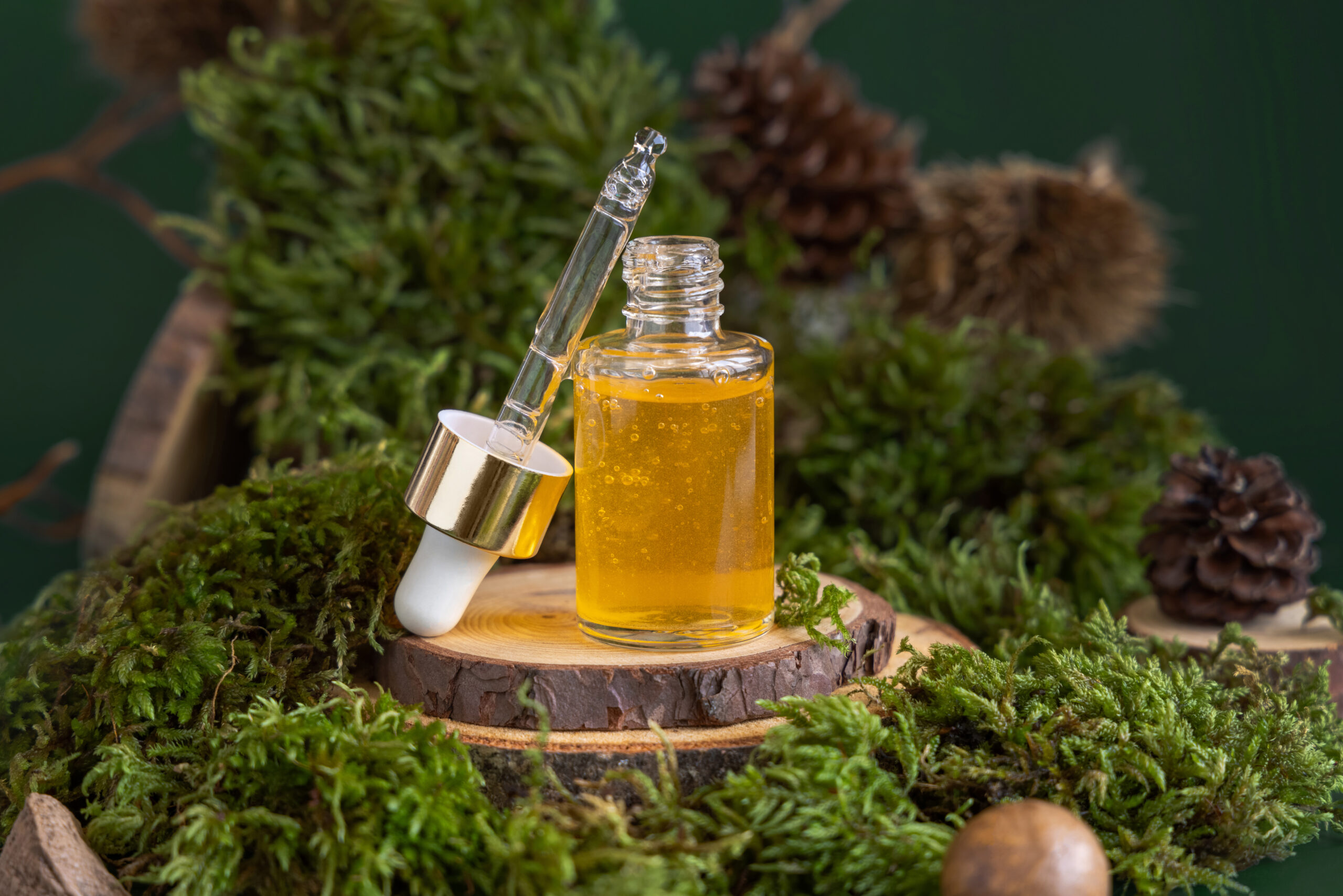 Opened dropper bottle with yellow liquid near green moss, close